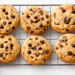 Stack of chewy chocolate chip cookies with melted chocolate chunks on a cooling rack